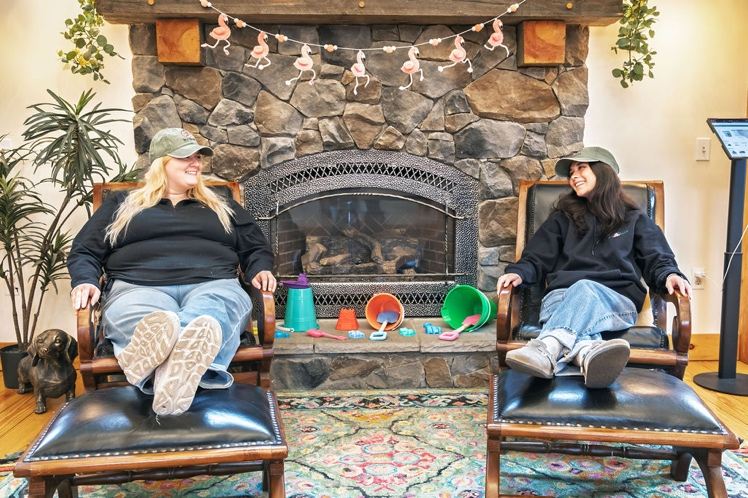 Two Bud Barn staff members relaxing in armchairs by the stone fireplace